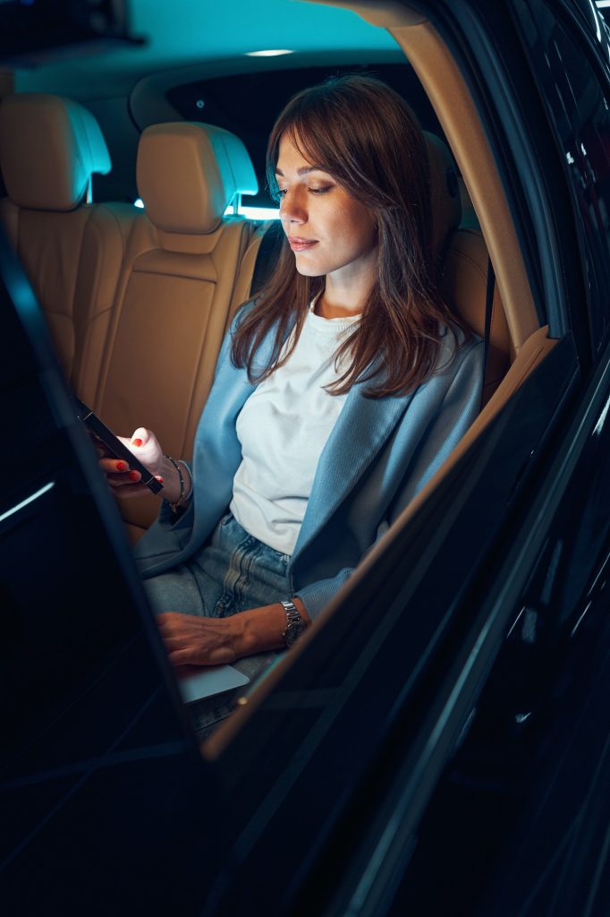 Woman sitting in automobile and using smartphone